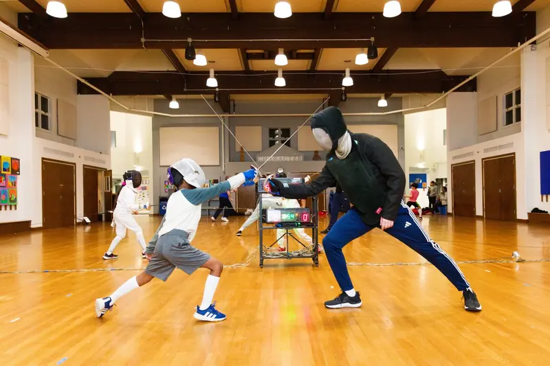 A fencing piste in a gym, lit for an evening class.